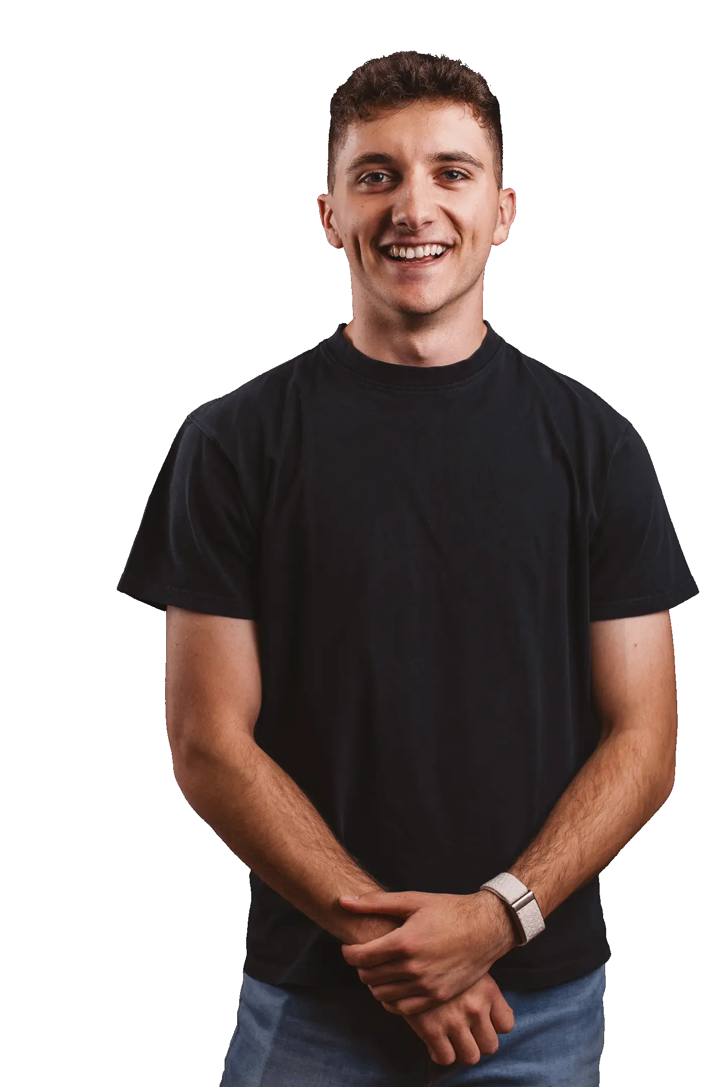 Junger Mann mit kurzen braunen Haaren lächelt, trägt schwarzes T-Shirt, blaue Jeans und eine Smartwatch.