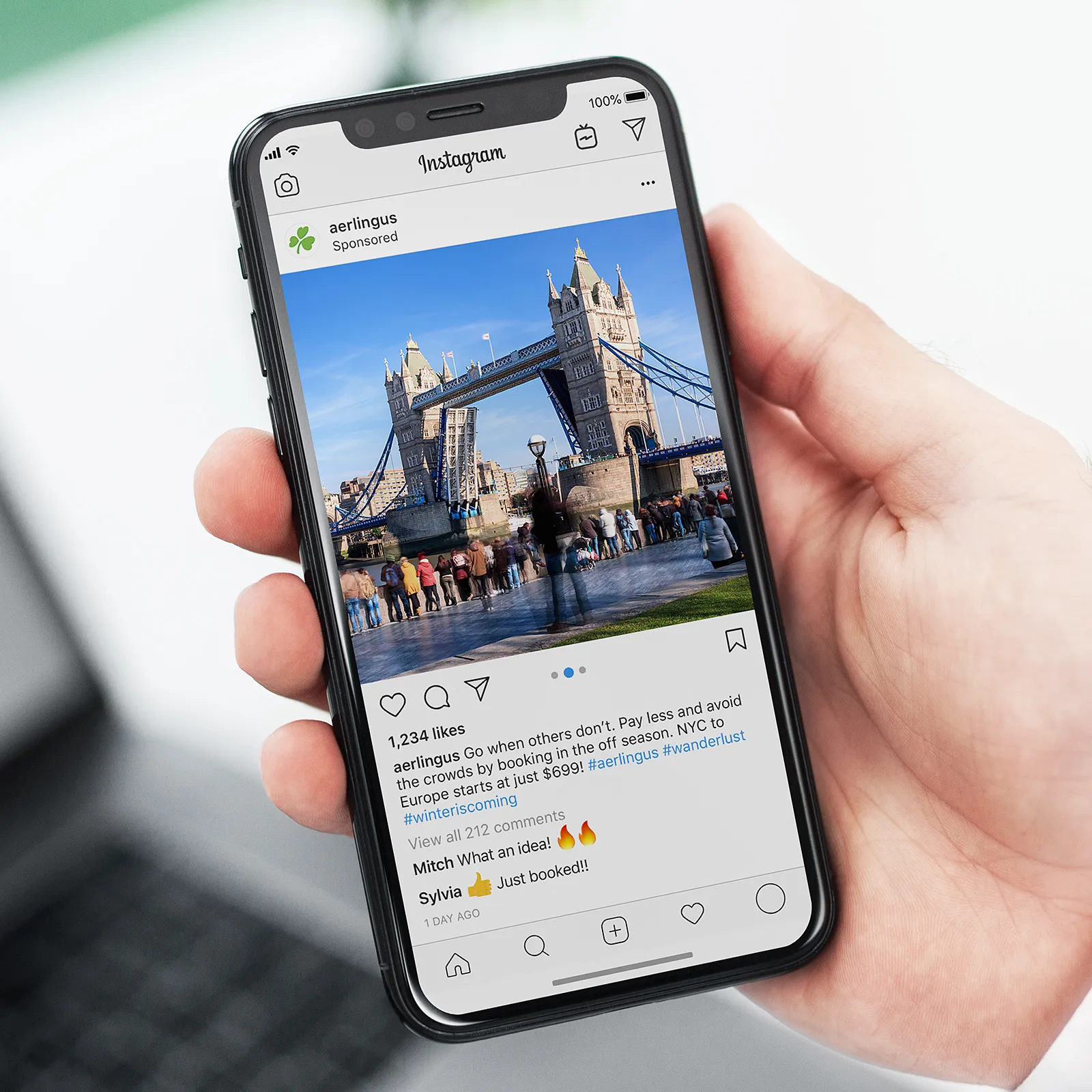 Hand holding smartphone displaying an Instagram post with a photo of Tower Bridge in London and a travel promotion by Aer Lingus.