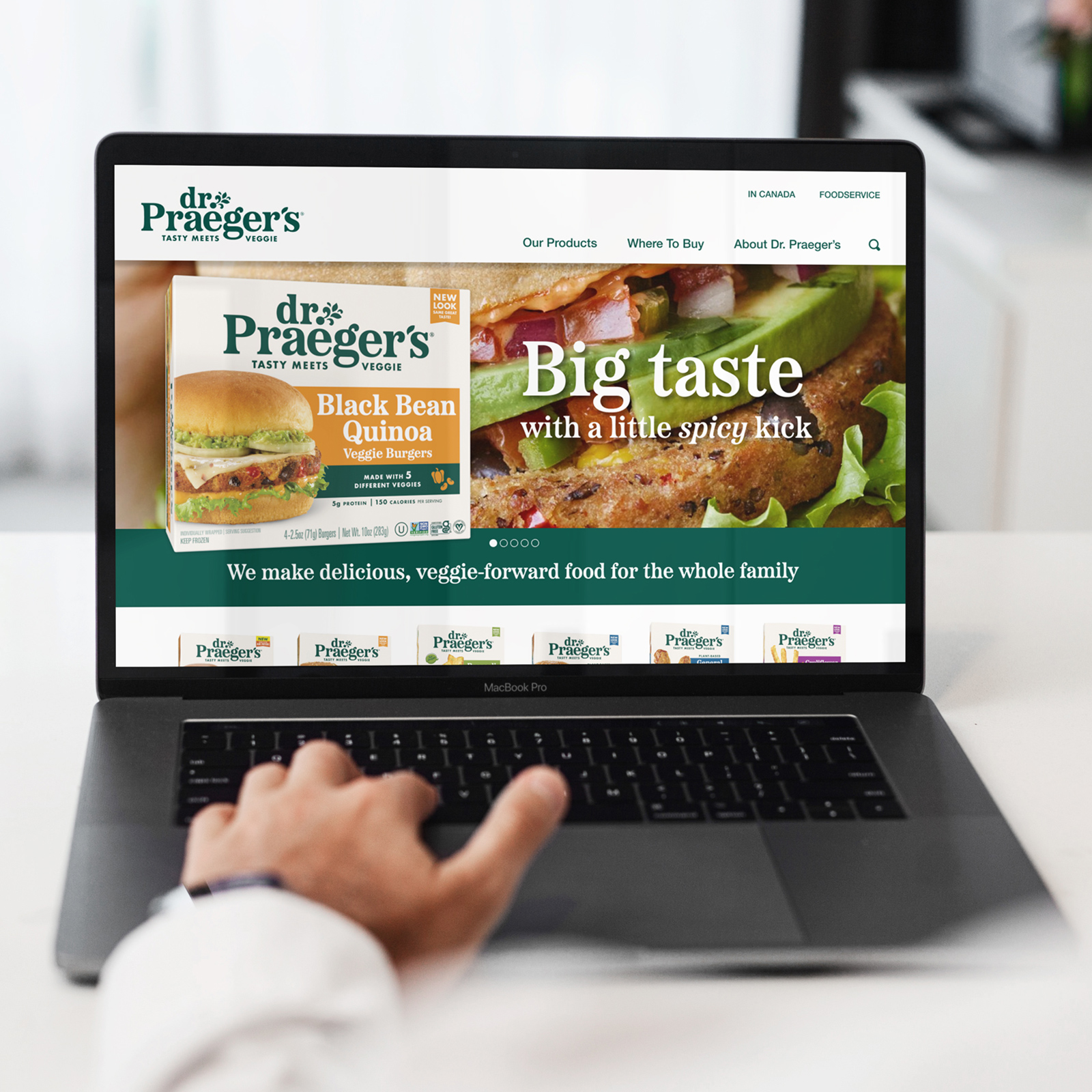 Person browsing Dr. Praeger's website on a MacBook Pro displaying Black Bean Quinoa Veggie Burgers with the slogan 'Big taste with a little spicy kick.'