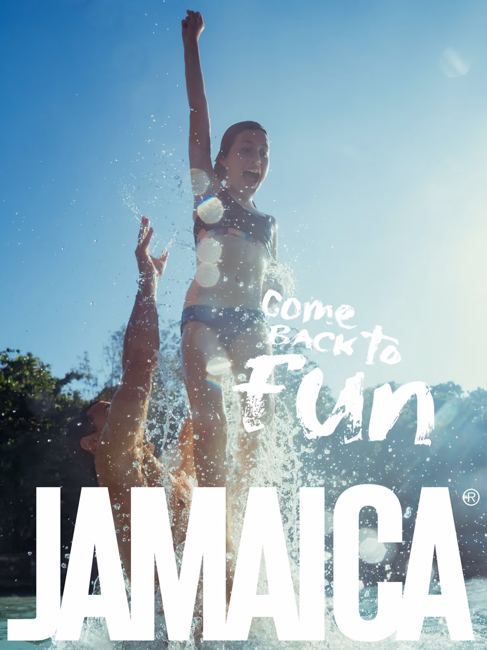 Child joyfully splashing in water, lifted by adult, with blue sky and text saying Come Back to Fun Jamaica.
