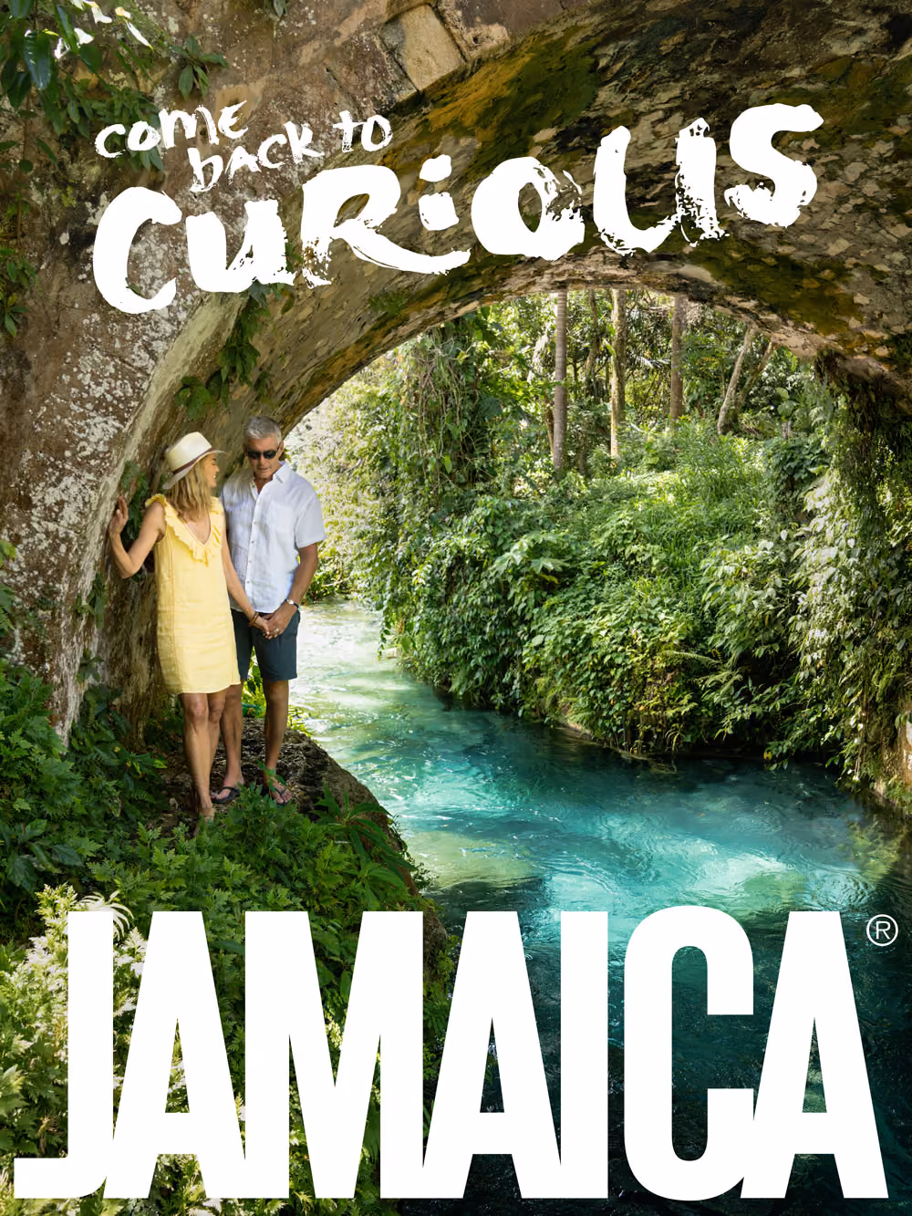 Couple holding hands under a stone arch by a clear blue river surrounded by lush green plants.