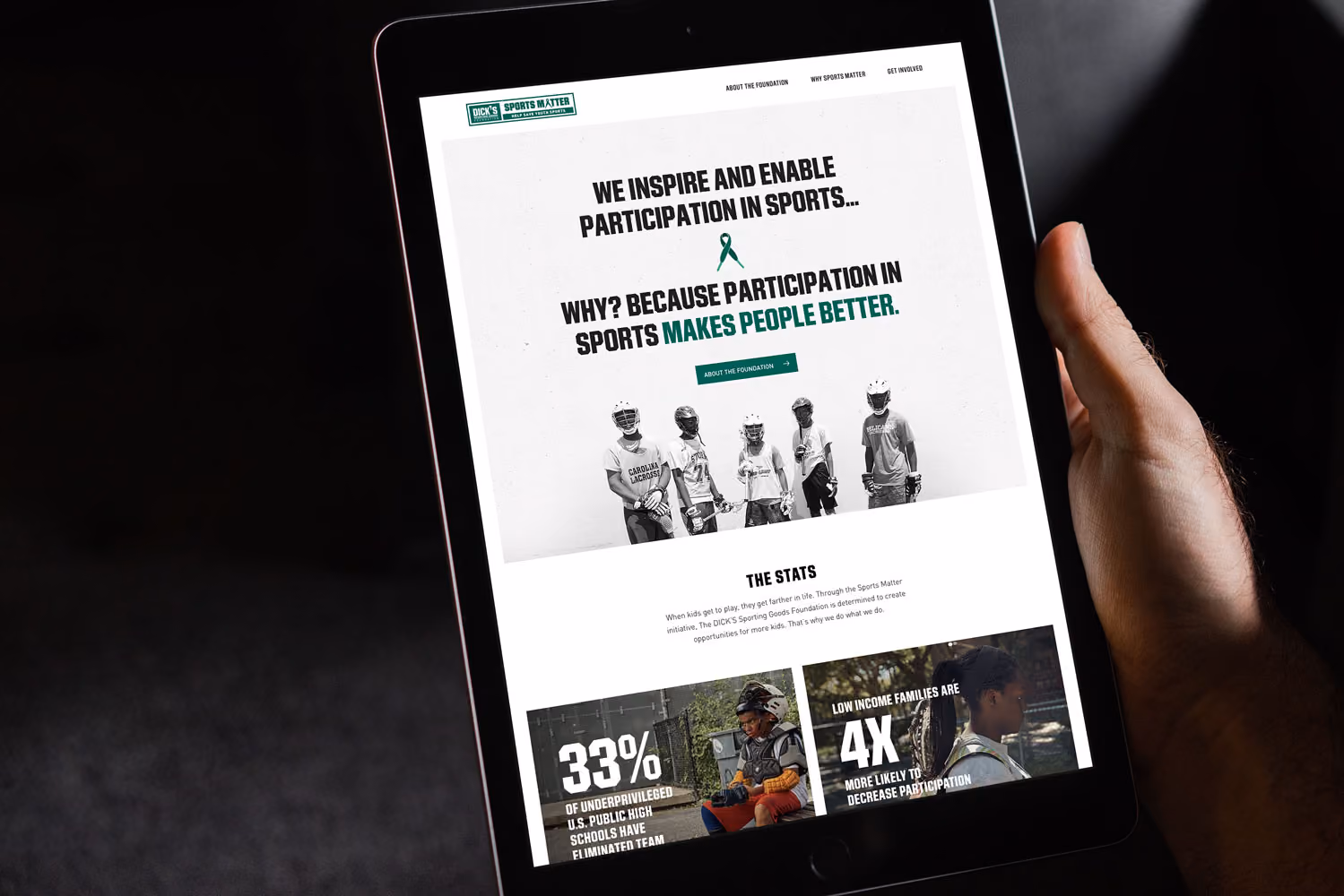 Hand holding a tablet showing a sports foundation website with youth lacrosse players and participation stats.