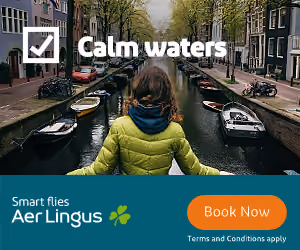 Person in green jacket facing canal with boats and row of buildings, text Calm waters Aer Lingus.