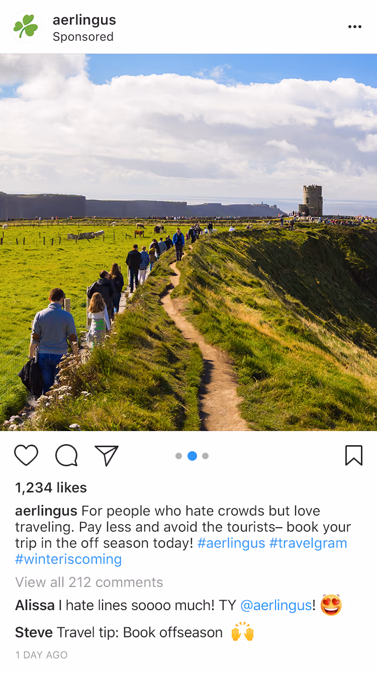 People walking along a narrow grassy path at cliffs with a stone tower in the distance under a blue sky.
