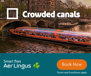 Tour boat with many passengers cruising a canal lined with historic brick buildings and a stone arch bridge in the background.