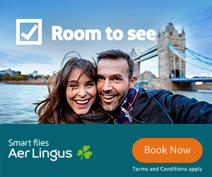 Smiling couple taking a selfie near the Tower Bridge in London with text 'Room to see' and an Aer Lingus advertisement offering 'Smart flies' and a 'Book Now' button.
