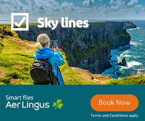 Person with backpack and blue jacket taking a photo of the Cliffs of Moher with a smartphone under a partly cloudy sky, alongside an Aer Lingus ad with text 'Sky lines' and a Book Now button.