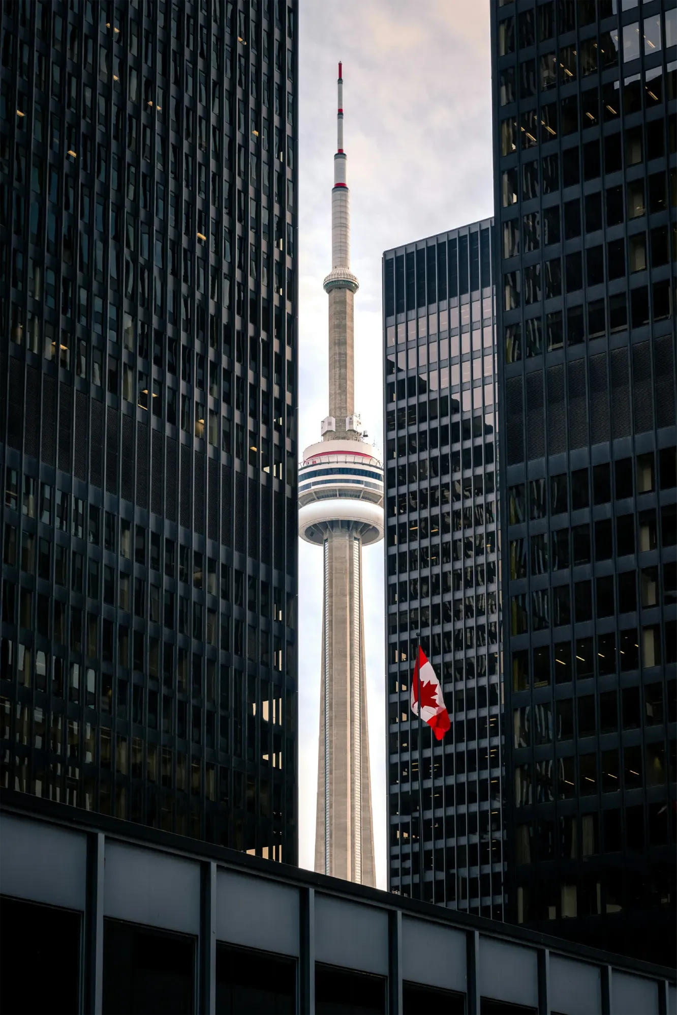 The CN Tower framed between two dark glass skyscrapers with a Canadian flag visible on the right building.