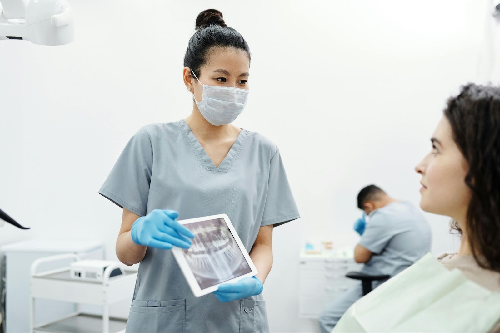A patient is looking at her dentist with nervous anticipation. The dentist is holding an X-ray, making direct eye contact over her mask while explaining the results.