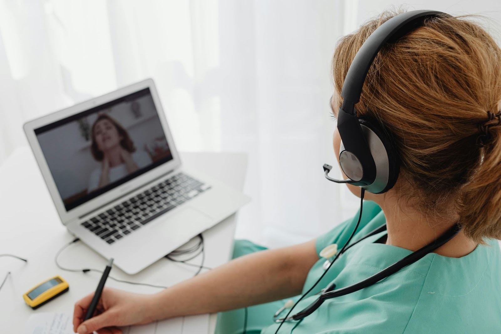 Picture of a doctor having a video call with a patient, who seems to be struggling with neck pain: she's rubbing her neck visibly.