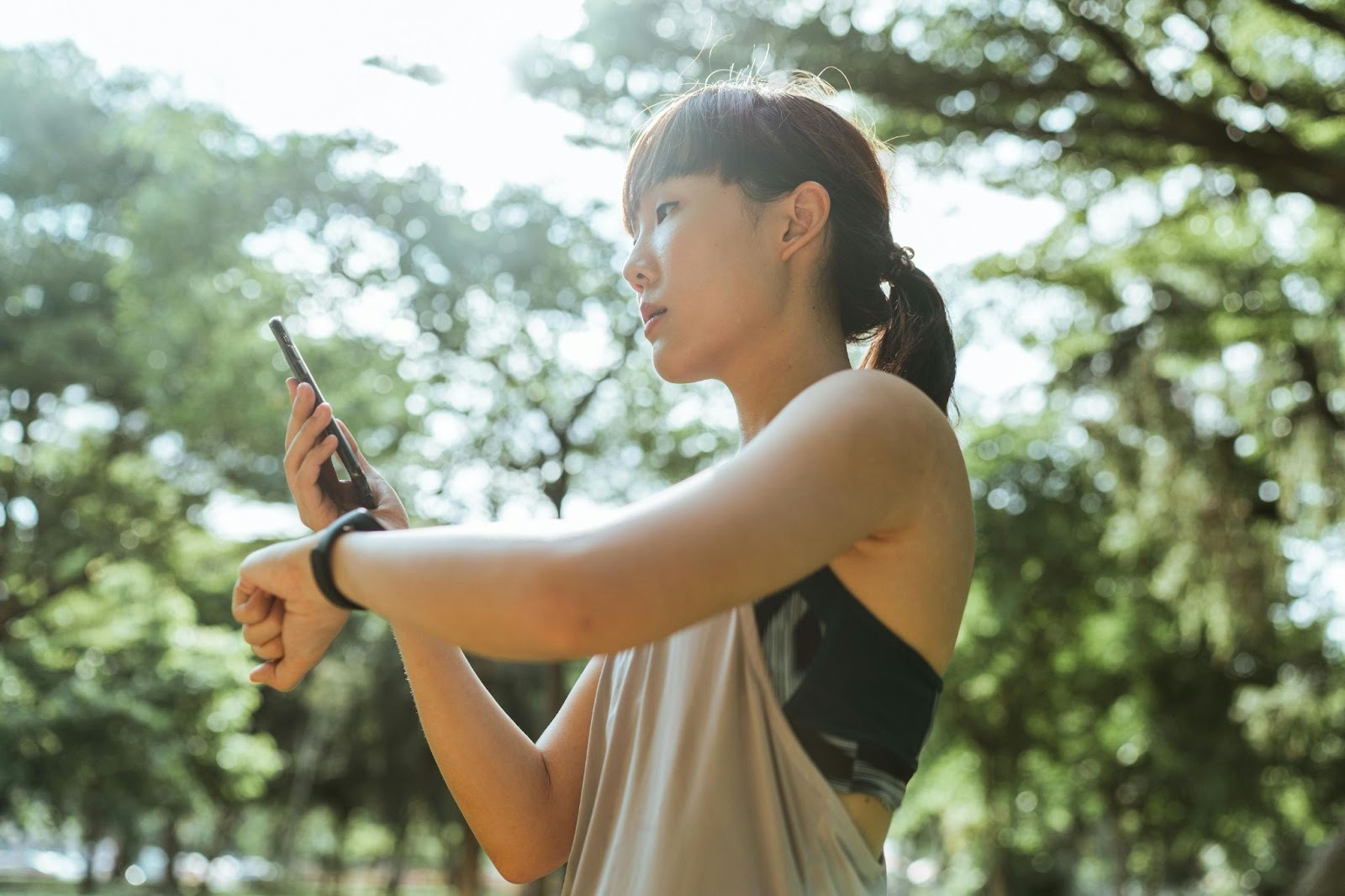 A health-conscious woman, dressed for running, is cross-referencing her smartwatch and her phone to see the results of her exercise.