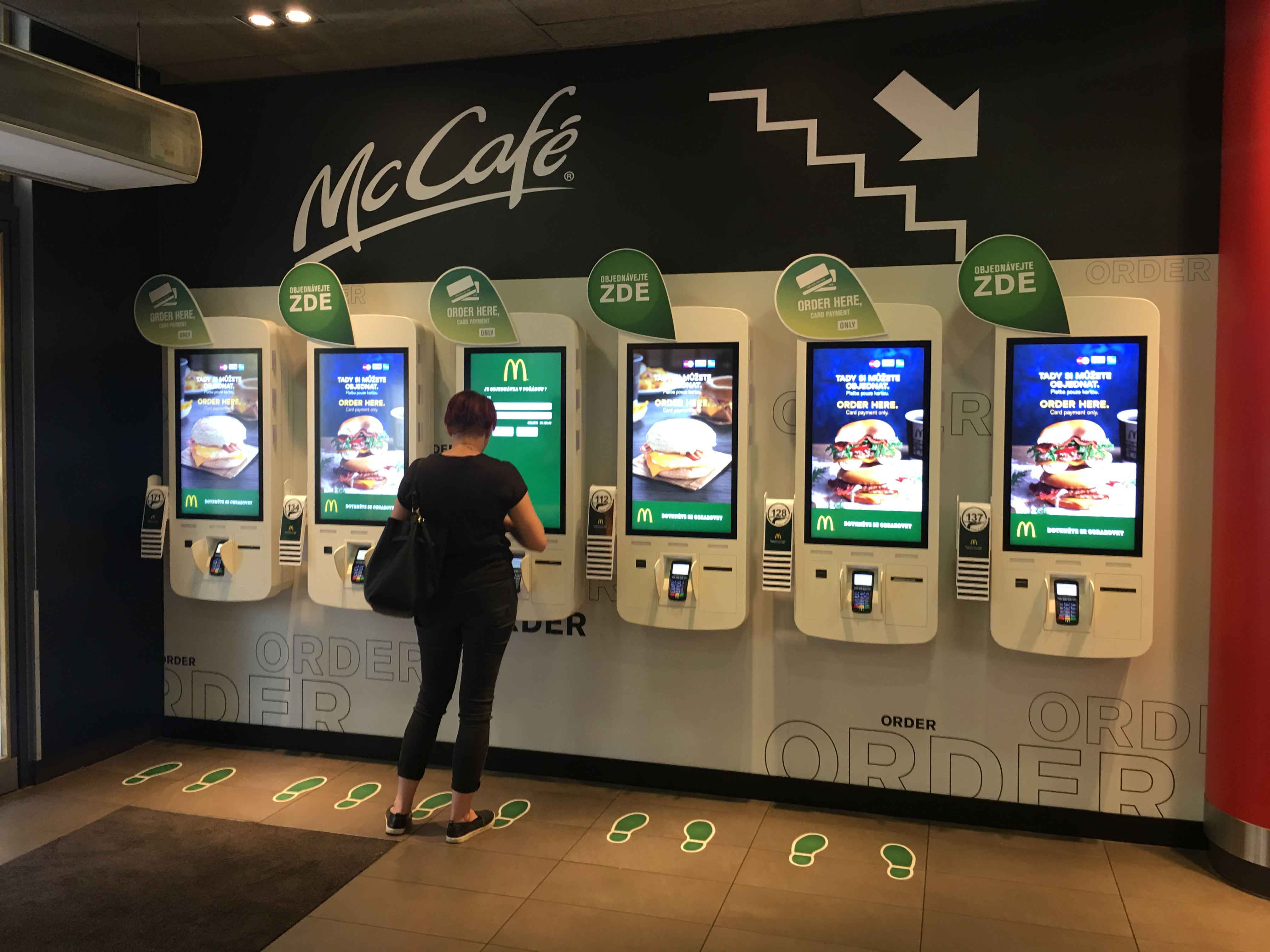 A woman placing an order in a line of self-order McDonald's kiosks