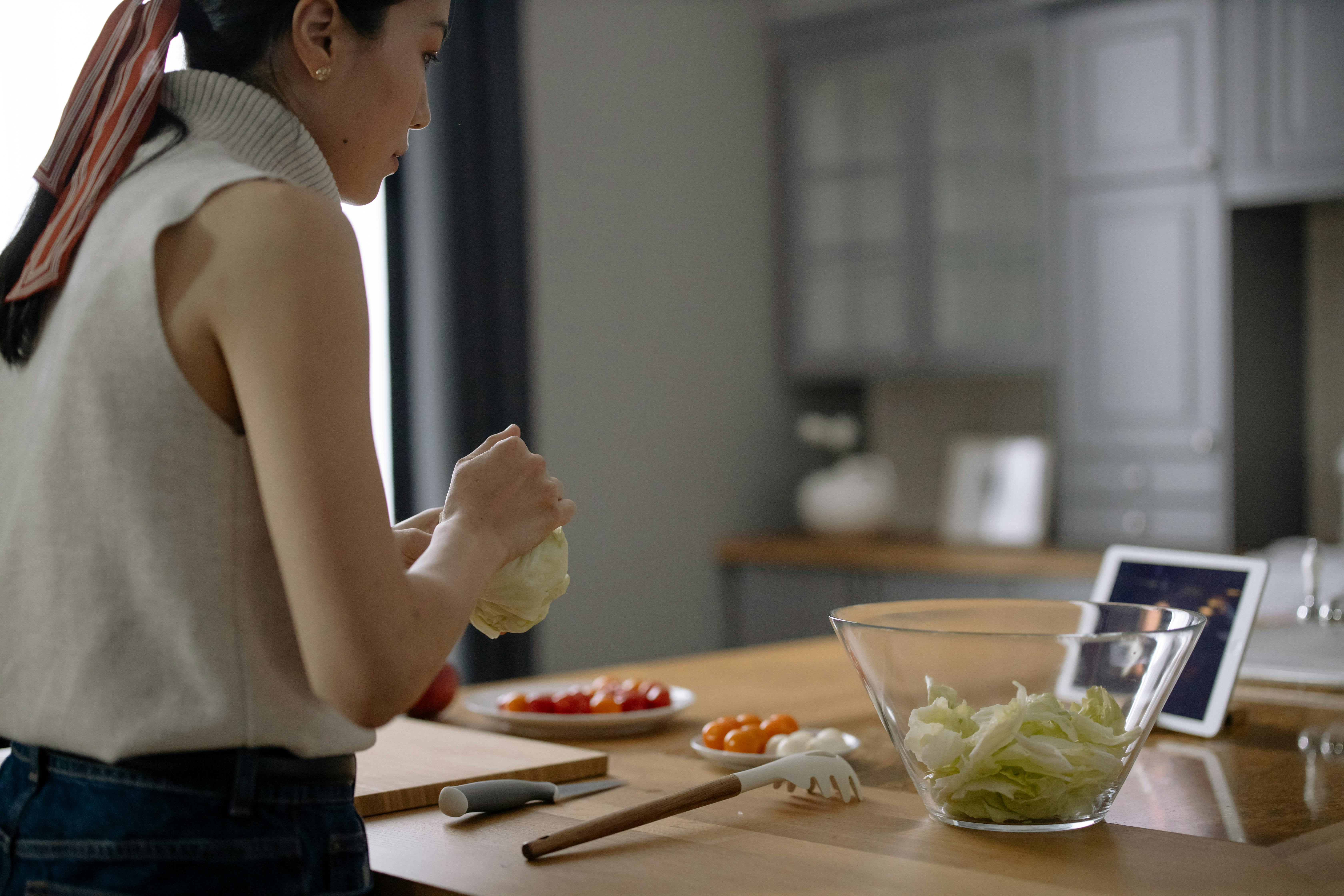 A woman watching a show on her tablet while chopping vegetables