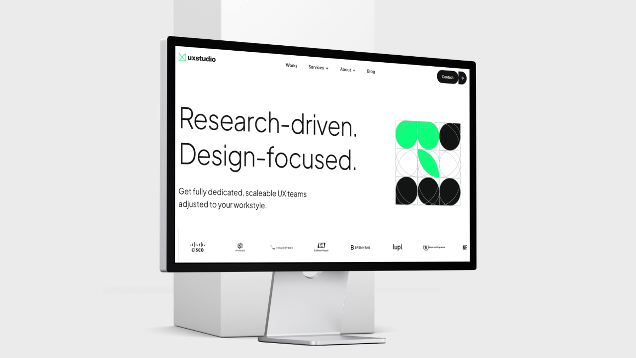 A computer monitor displaying the ux studio homepage with the text "Research-driven. Design-focused."