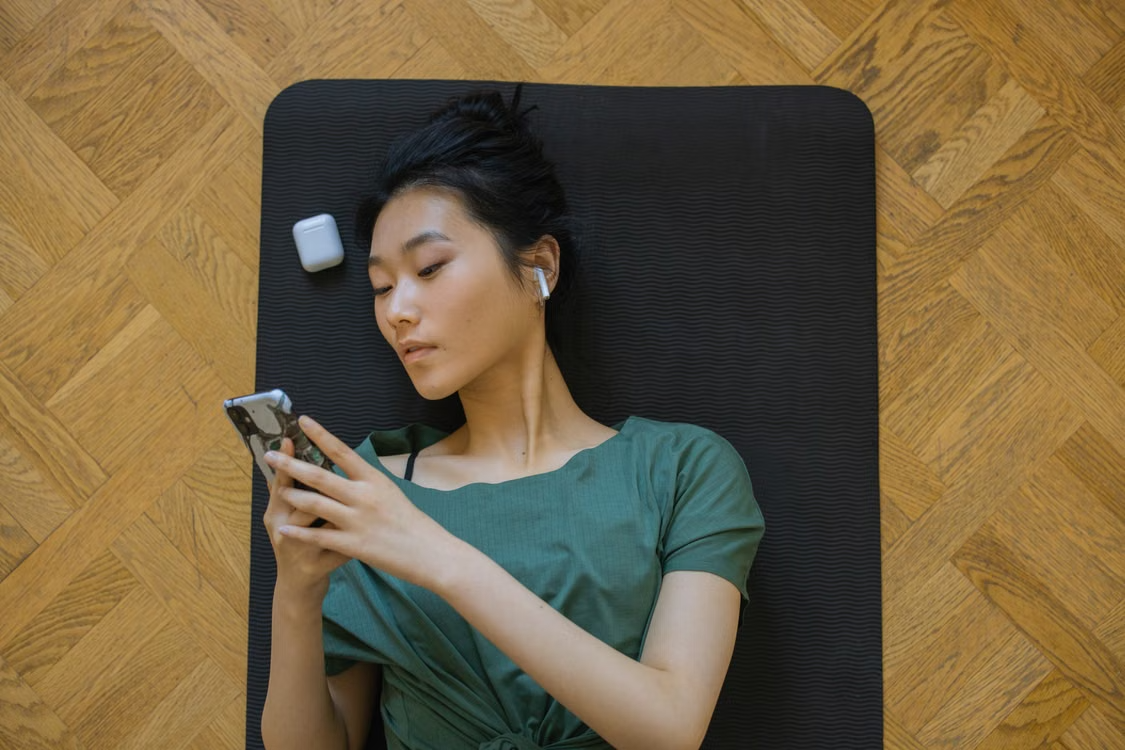 Woman using a phone while lying on a yoga mat.