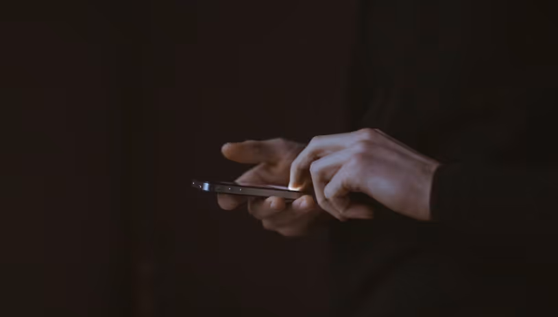 Nahaufnahme von Händen, die mühsam auf einem Smartphone tippen, vor dunklem Hintergrund, symbolisiert die Frustration von Nutzern bei einer schlechten mobilen Website. upgreight, die Webflow Agentur Südtirol, verhindert diese mobile Katastrophe durch Responsive Design.