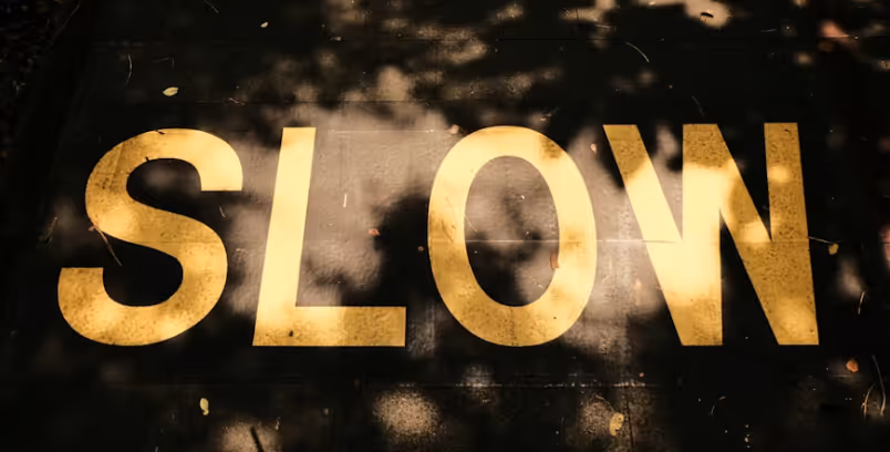 Das Wort „SLOW“ in großen gelben Buchstaben auf dunklem Asphalt markiert; eine visuelle Metapher für langsame Website-Ladezeiten, die Konversionen verhindern. Die Webflow Agentur Südtirol upgreight optimiert den PageSpeed für maximale Performance.