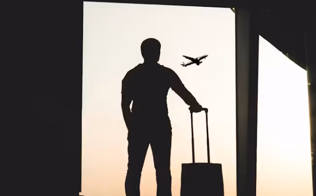 Silhouette eines Reisenden mit Rollkoffer am Fenster, die die Abhängigkeit von OTAs und den Mangel an Direktbuchungen bei Hotels mit veraltetem Webdesign Hotel visualisiert.