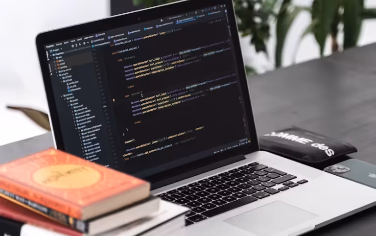 Ein geöffneter Laptop auf einem Schreibtisch zeigt JavaScript-Code für eine Webflow-Entwicklung. Daneben liegen Bücher und ein Smartphone.