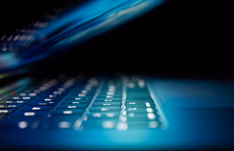Nahaufnahme einer blau beleuchteten Laptop-Tastatur im Dunkeln als Symbolbild für Cybersicherheit, Programmierung und IT-Infrastruktur.