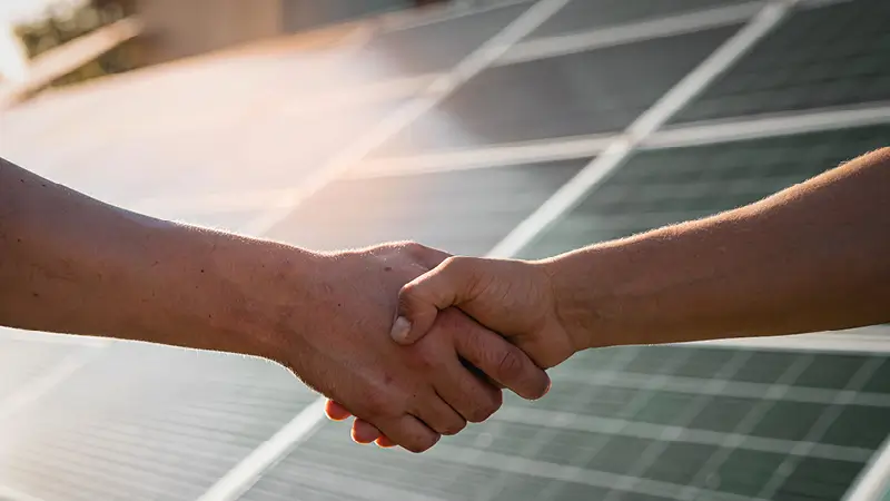 Zwei Personen vor einer Photovoltaikanlage, die sich die Hände reichen