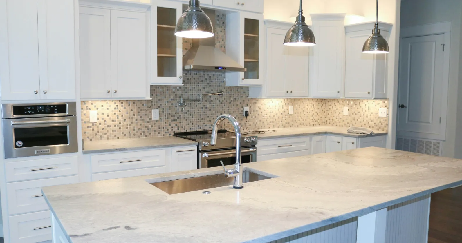 Modern kitchen with white cabinets, mosaic tile backsplash, stainless steel appliances, and a large island.