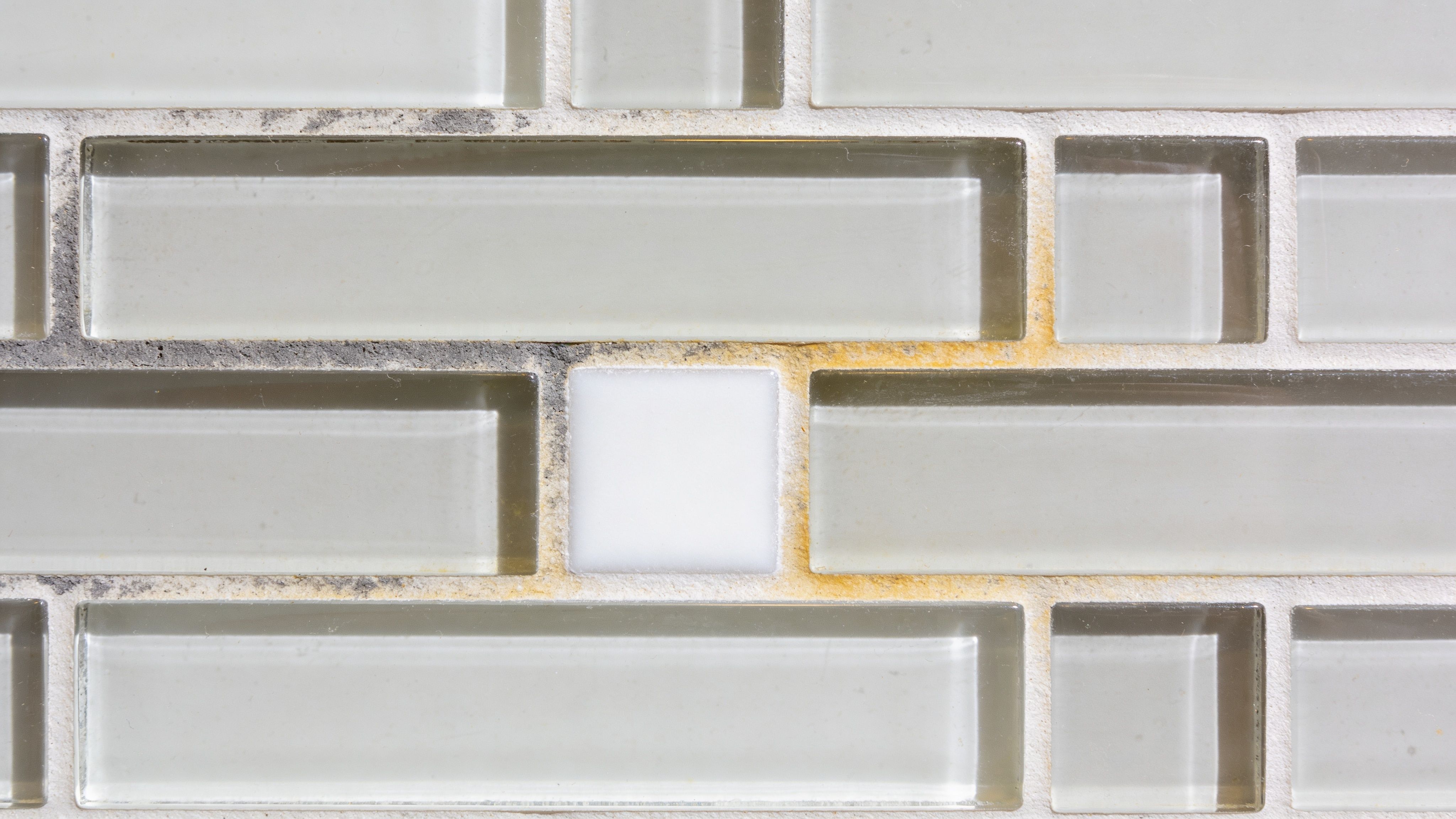 Close up of a decorative wall tile pattern with clean white grout surrounding glass and solid pieces.