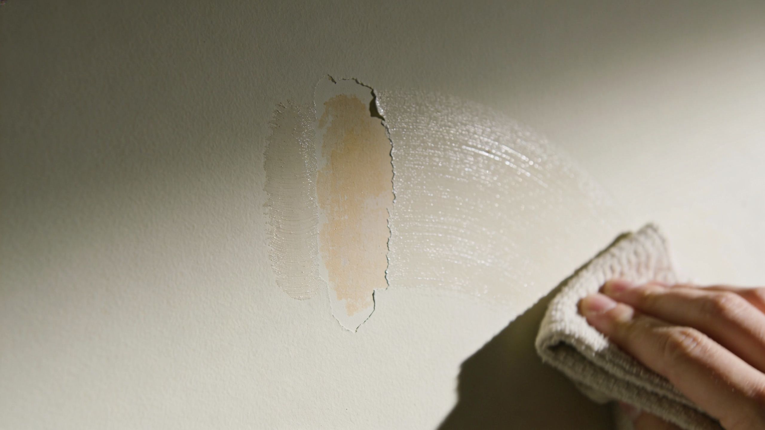 A close-up view of a person cleaning a damaged matte painted wall with a cleaning cloth.