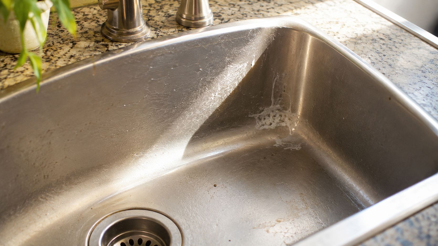 A stainless steel kitchen sink showing a white crusty mineral buildup deposit along the interior side wall.
