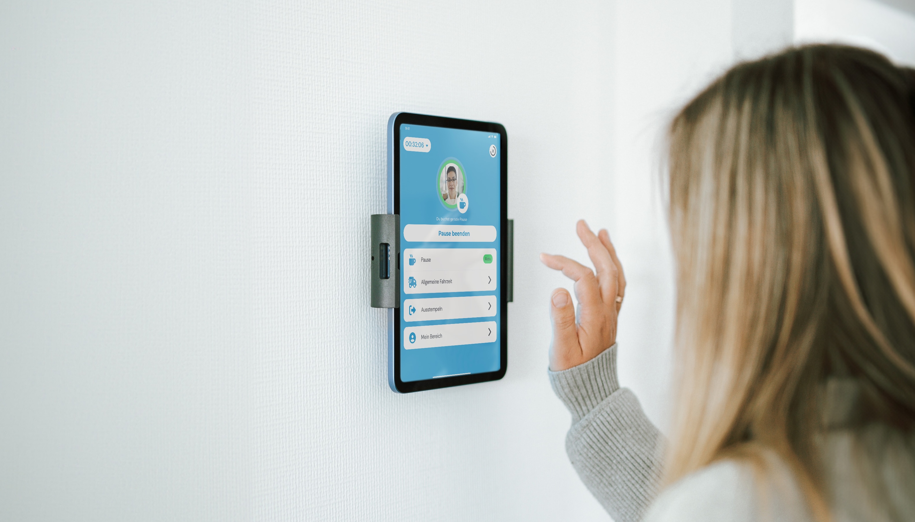 Frau nutzt ein an der Wand befestigtes Tablet-Terminal zur digitalen Zeiterfassung mit der clockin-App.
