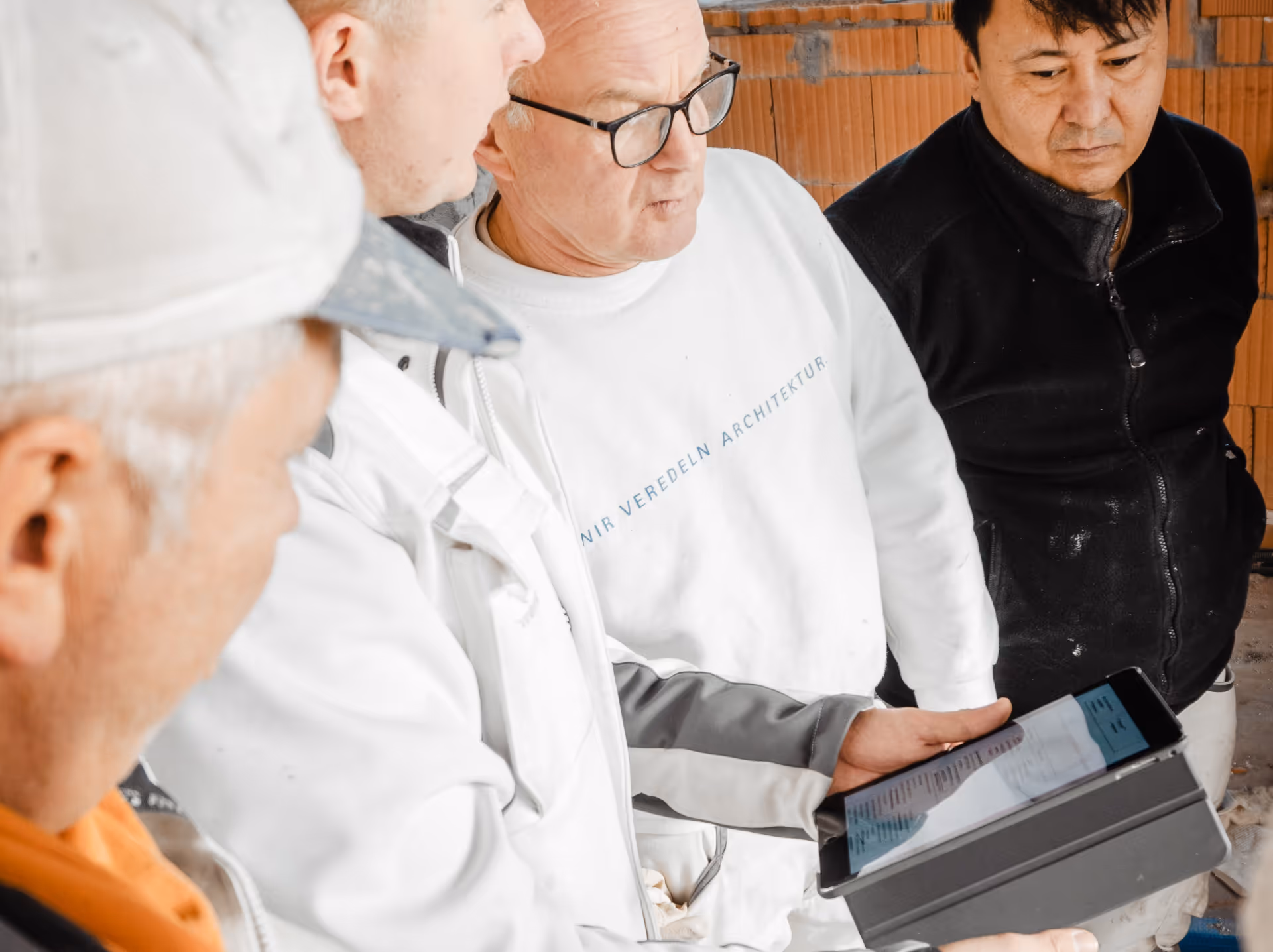 Vier Handwerker besprechen Baupläne auf einem Tablet in einem Rohbau