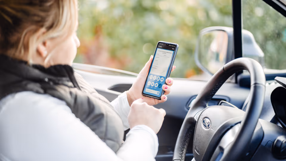 Mitarbeiterin erfasst Arbeitszeit mit der clockin-App auf dem Smartphone im Auto – digitale Zeiterfassung unterwegs.