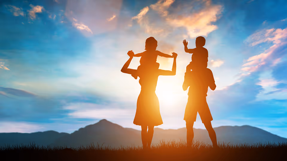 Silhouette einer Familie im Sonnenuntergang – Mutter und Vater tragen jeweils ein Kind auf den Schultern, während sie gemeinsam die Natur genießen.