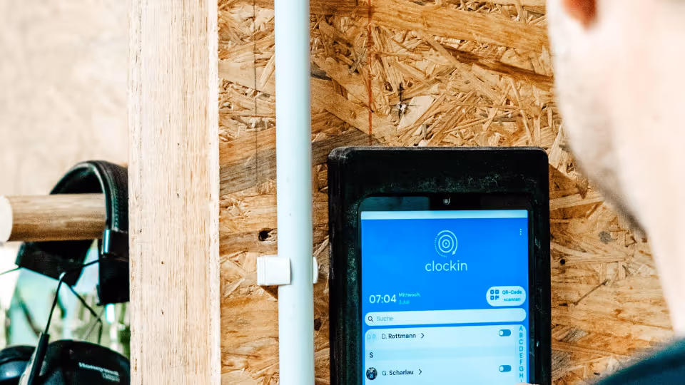 Mitarbeiter erfasst seine Arbeitszeit an einem Wandtablet mit der digitalen Zeiterfassungs-App clockin in einer Werkstatt.