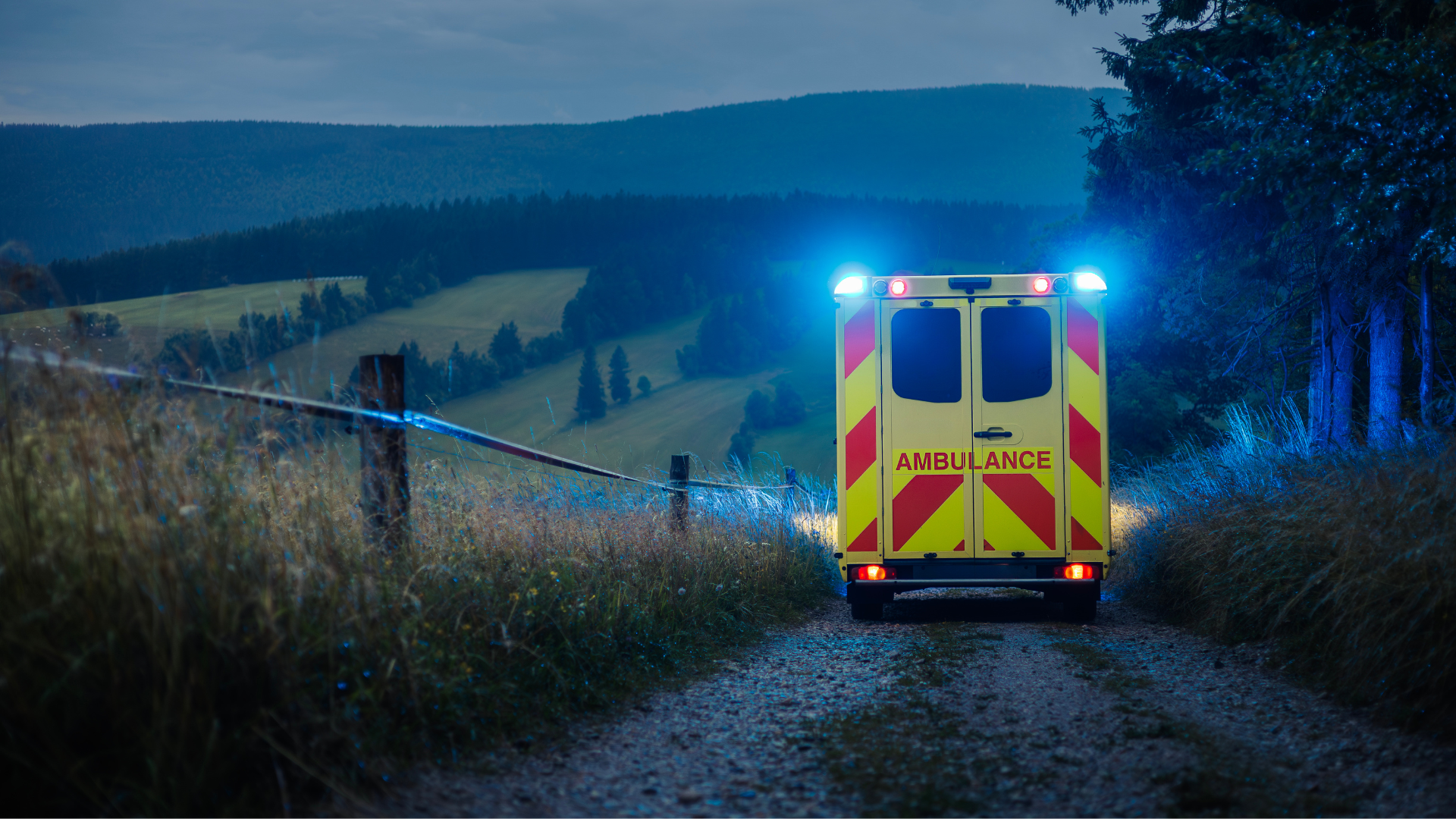 Rückansicht eines Rettungswagens mit eingeschaltetem Blaulicht auf einem abgelegenen Feldweg bei Dämmerung; symbolisiert den unermüdlichen Einsatz im Rettungsdienst während einer 24 Stunden Schicht.