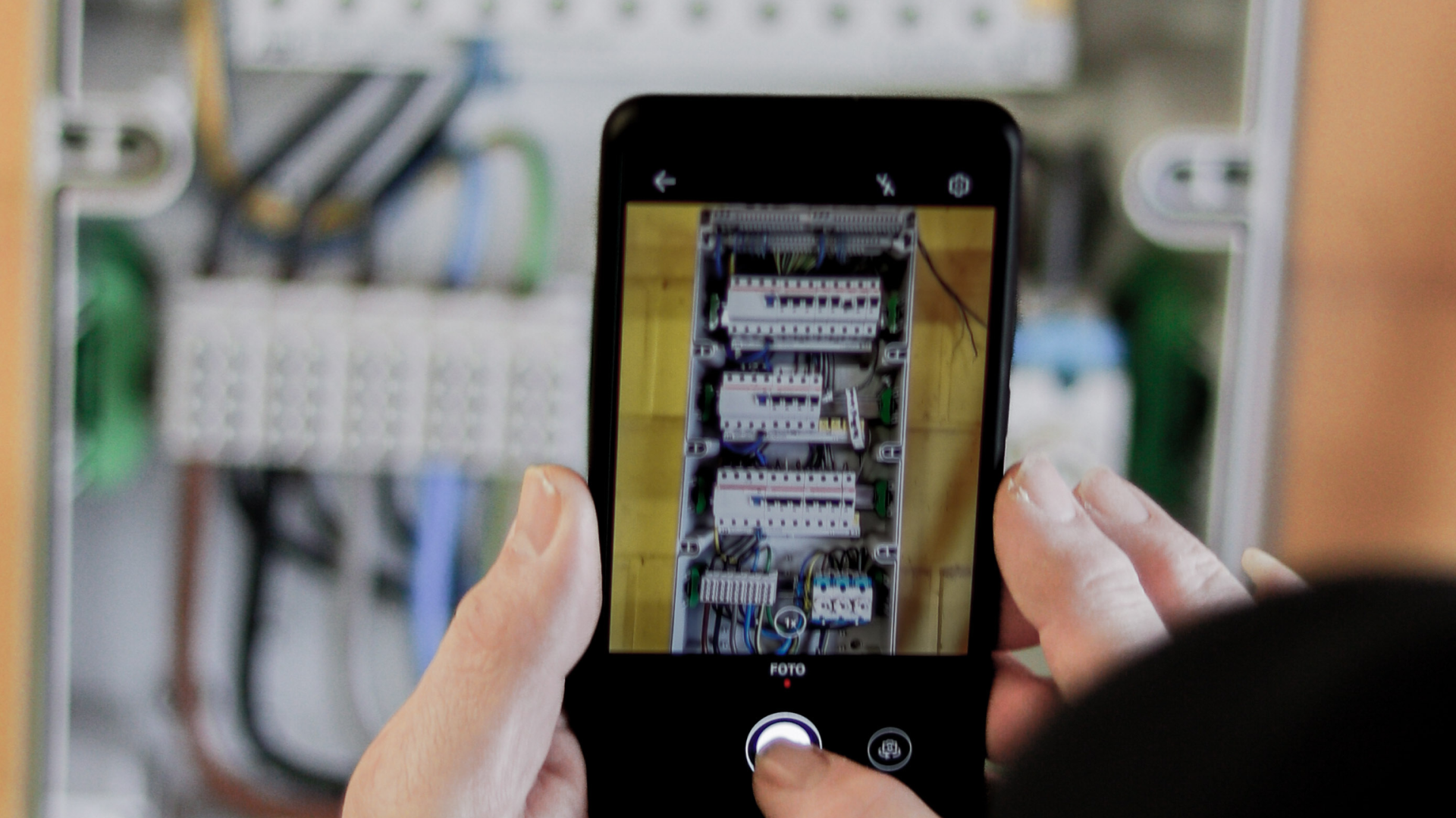 Elektrotechniker macht mit einem Smartphone ein Foto von einem Sicherungskasten zur digitalen Projektdokumentation