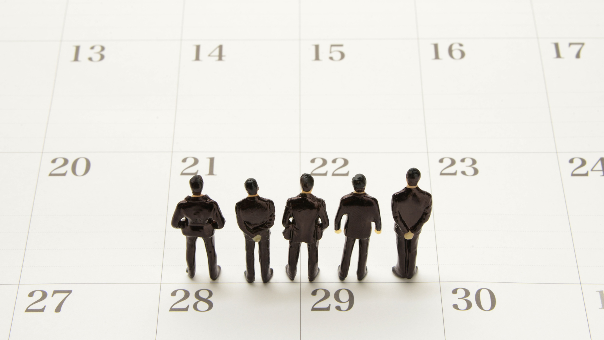 Fünf Figuren in Anzug stehen mit dem Rücken zur Kamera gestellt in verschiedenen Posen auf einem Kalenderblatt