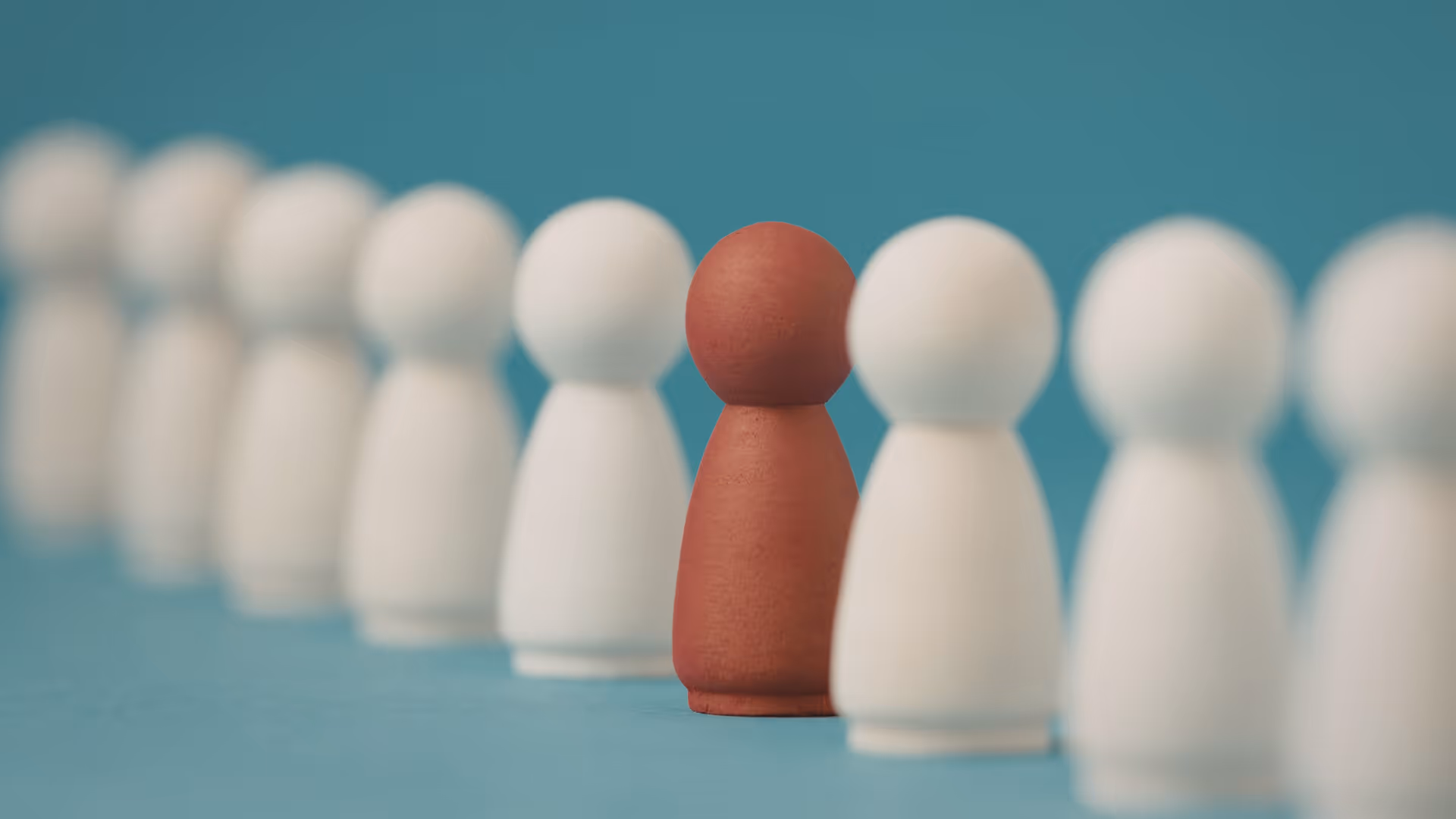 Eine Reihe weißer Spielfiguren, eine einzelne ist rötlich. 