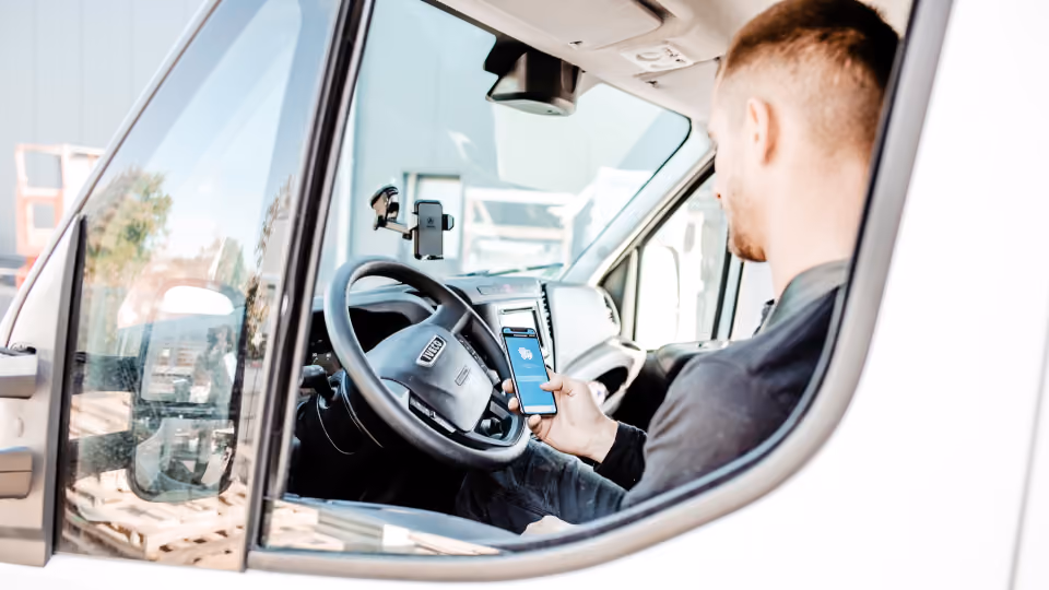 Handwerker sitzt in seinem Transporter und schaut während der Fahrt auf sein Smartphone, das am Lenkrad befestigt ist