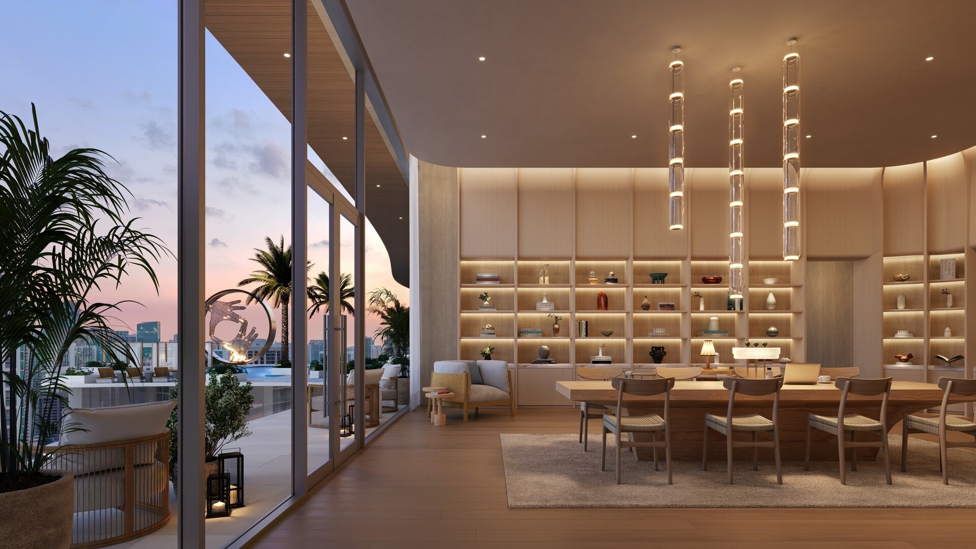 Modern co-working lounge with wooden table and chairs, illuminated shelves, and outdoor terrace with palm trees at sunset.