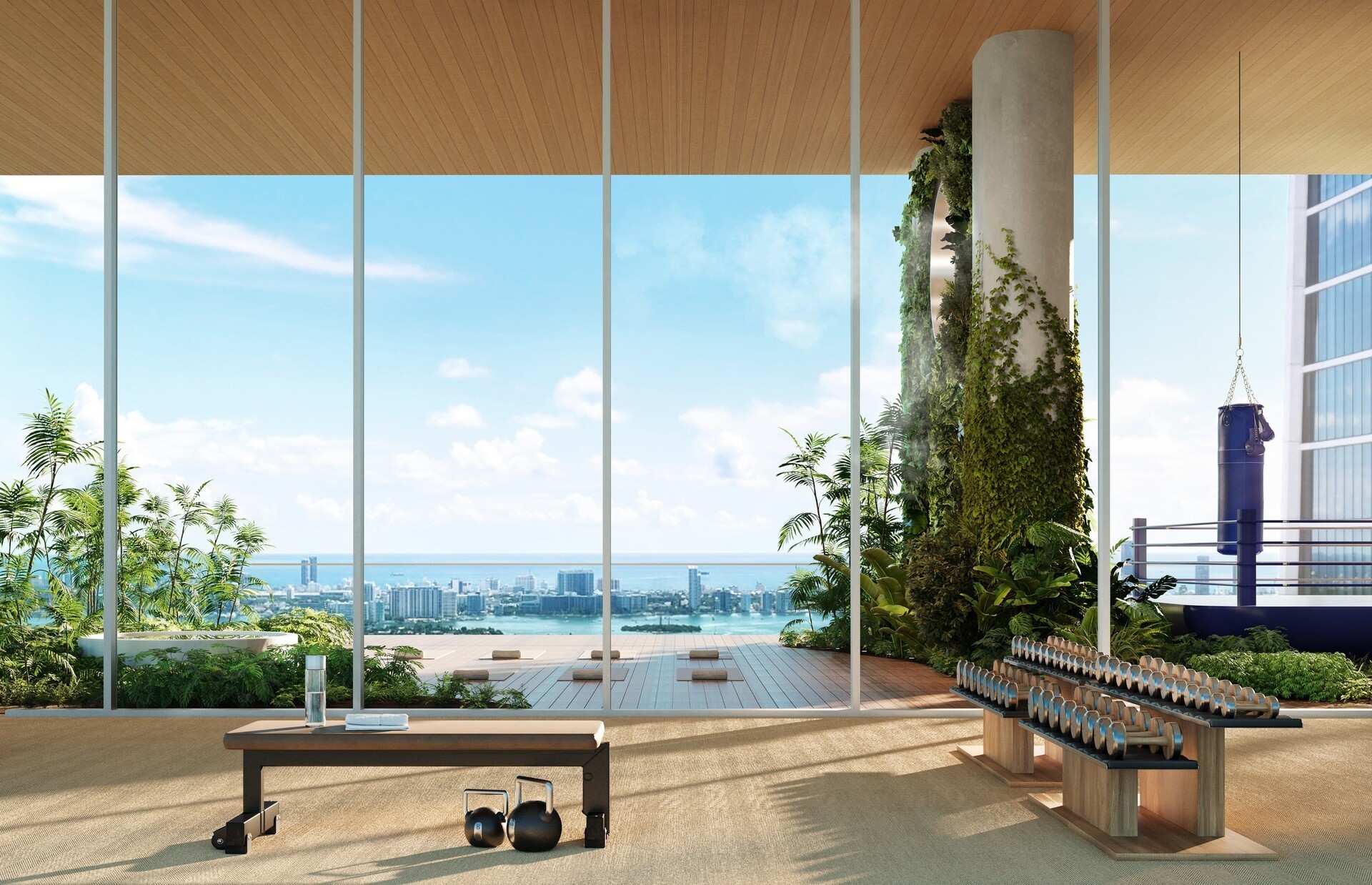 Modern fitness room with dumbbells, kettlebells, bench, punching bag, large windows showing city skyline and ocean view.