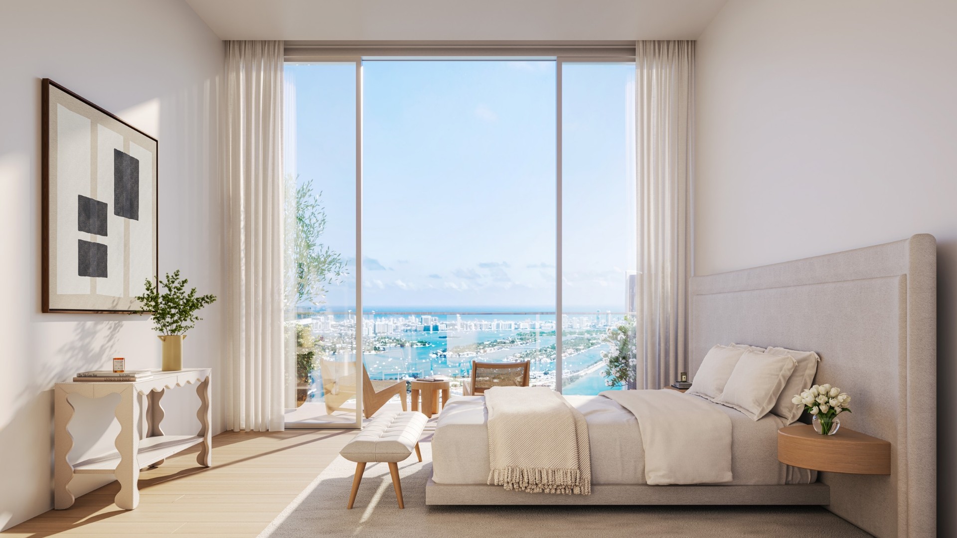Minimalist bedroom with beige bed, bench, side table with flowers, console table, abstract wall art, and large floor-to-ceiling windows showing a city and ocean view.