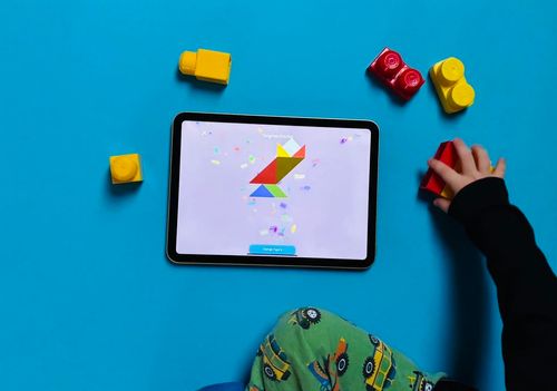 A photo of a toddler boy playing with his toys and the tangram puzzles in the Toddlr tablet app