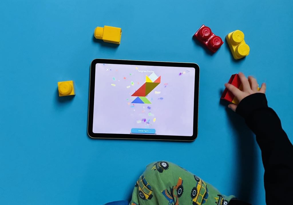 A photo of a toddler boy playing with his toys and the tangram puzzles in the Toddlr tablet app