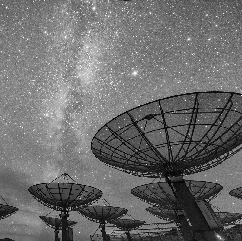 Black and white photo of multiple satellite dishes under a star-filled night sky.