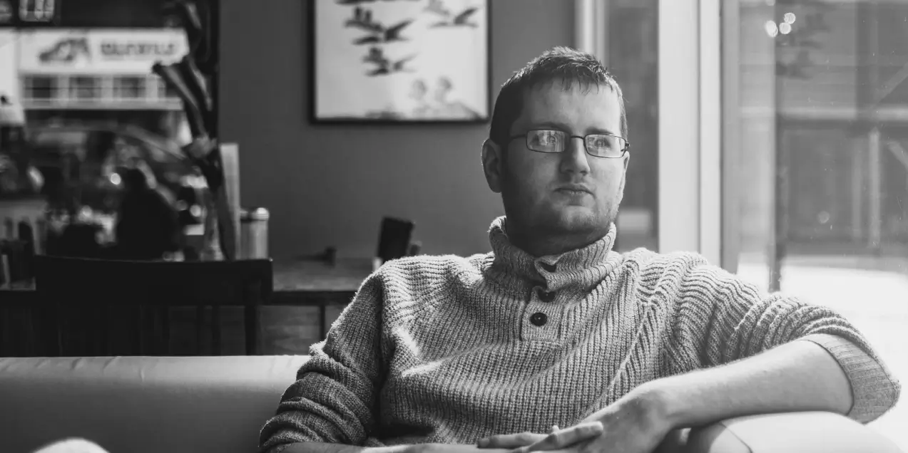  A man in glasses sitting on a couch, focused on On Demand Sales Training.
