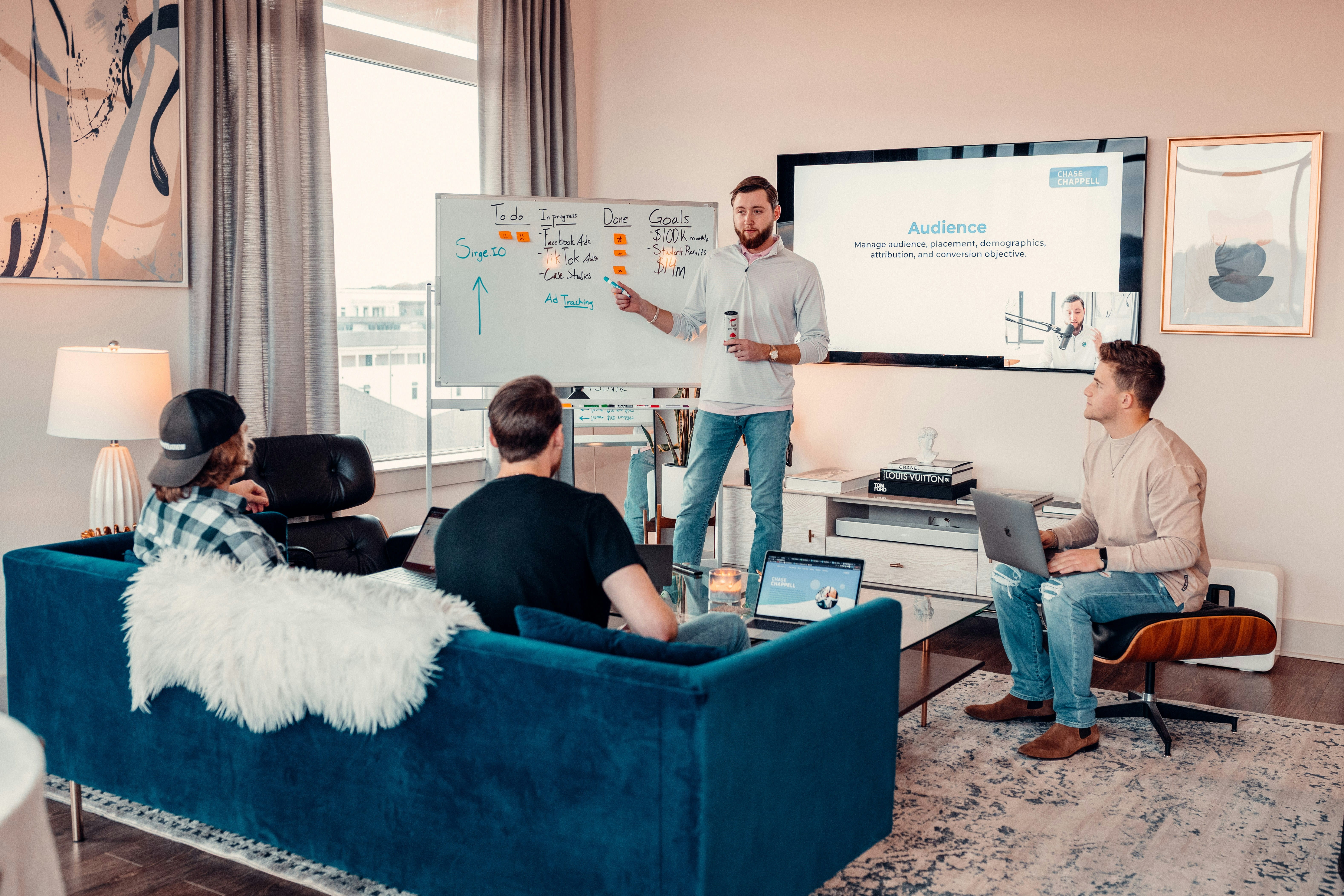 Presenter leading a sales and marketing training session with a small team, using a whiteboard and presentation screen in a modern office.
