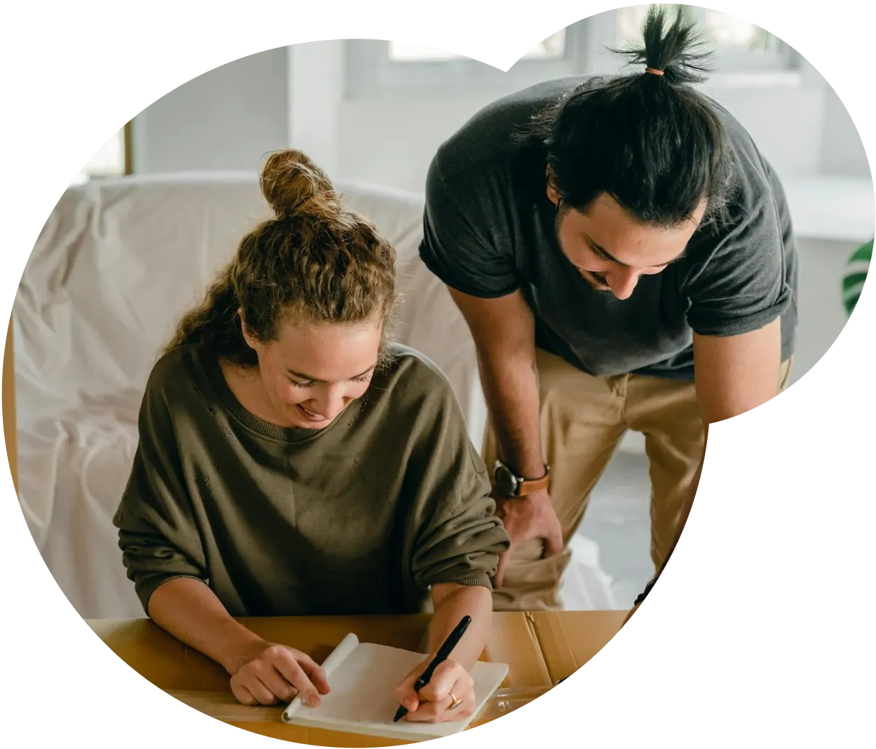 Man looking over a woman's shoulder as she works on a notebook on the desk in front of her.
