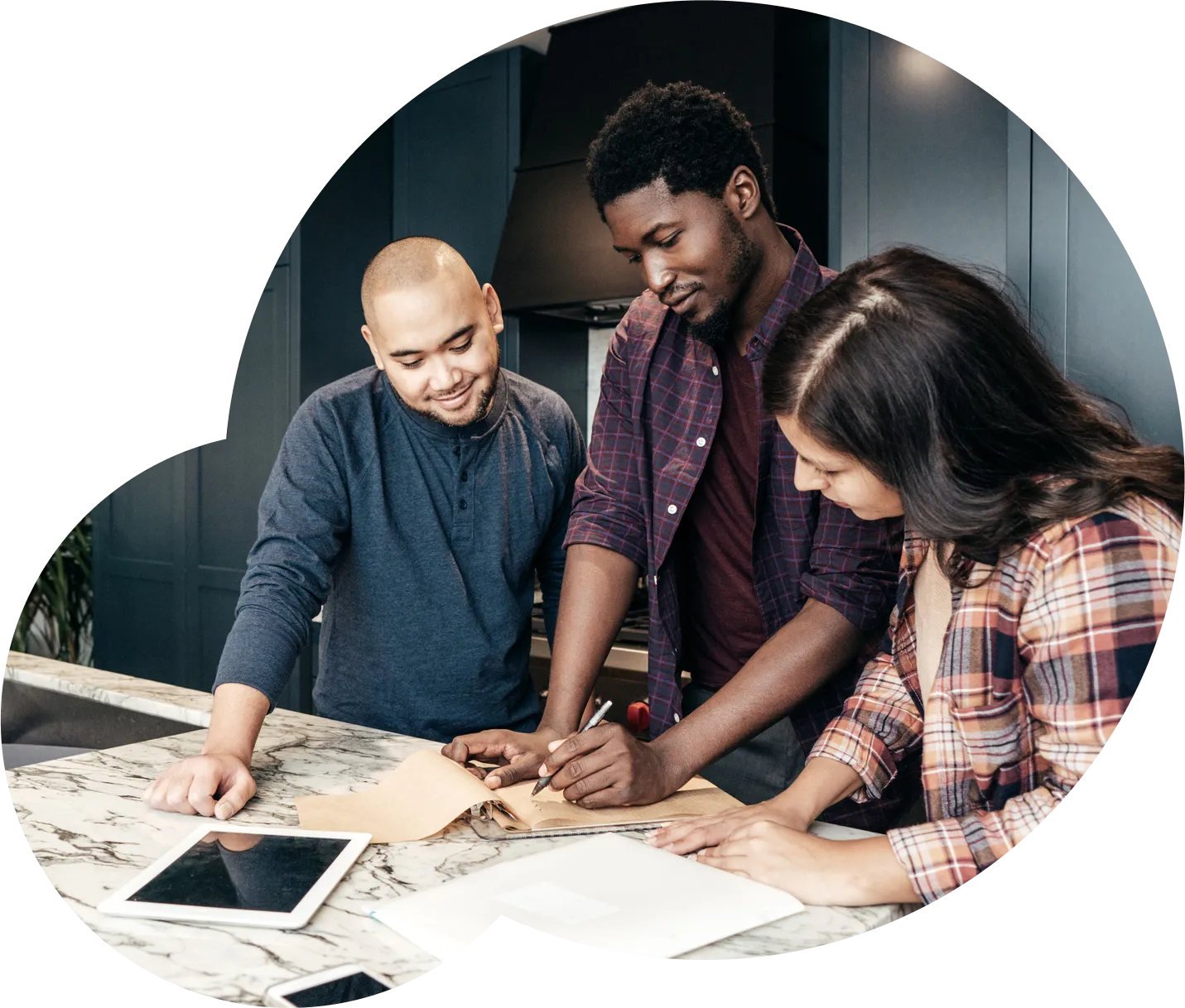 Three people standing in a kitchen, working on papers and files laid out in front of them.