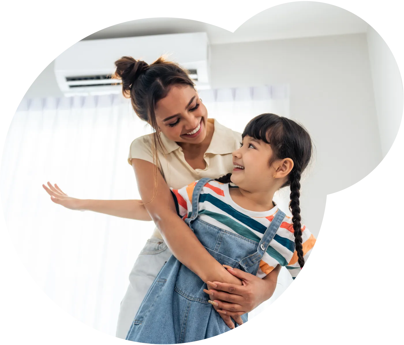 A young woman and girl standing in their home, hugging and smiling at each other.